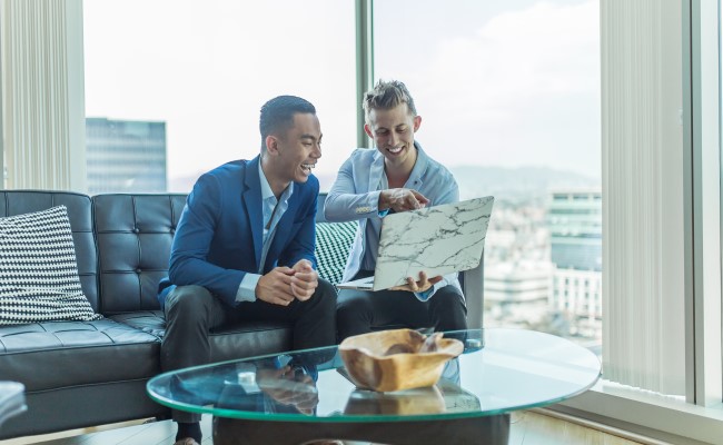 Two men chatting and laughing as they work together on a laptop problem showing the company culture.